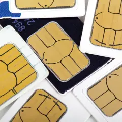 Zbliżenie na złote chipy kart SIM, ułożonych na białych plastikach i ciemnym tle. Każdy minisim gotowy do działania.