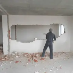 Mężczyzna z młotem burzy ścianę, tworząc otwór. Wokół leżą gruzy. To część remontu, gdzie powstanie nowy podciąg.