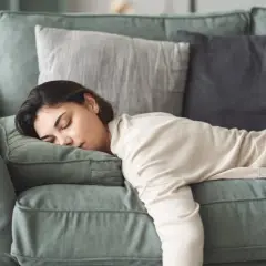 Eine Frau liegt erschöpft auf einem Sofa, ihre Augen sind geschlossen. Sie leidet unter Gliederschmerzen ohne Fieber und ruht sich aus.
