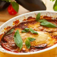 Aubergine parmigiana dorée et gratinée, garnie de feuilles de basilic frais. Un plat réconfortant prêt à être dégusté.