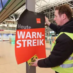 Ein Mann mit Warnweste befestigt ein Schild "Heute WARN-STREIK" an einem Pfosten. Hier wird heute gestreikt.