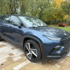 Nowy, granatowy Fisker SUV stoi na wybrukowanym podjeździe. W tle żółty i pomarańczowy samochód.