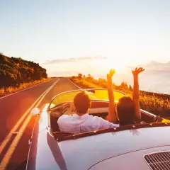 Coppia in auto decappottabile al tramonto, con le braccia alzate, godendosi un itinerario Croazia da sogno.