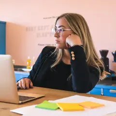 Kobieta w okularach zastanawia się, ile trwa staż z urzędu pracy, patrząc na laptopa. Na biurku kolorowe karteczki.