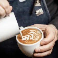 Barista skapar vacker latte art i en vit kopp. Mjölkskummet bildar ett mönster av virvlar.