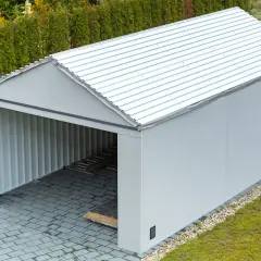 Nowoczesna wiata to budowla z metalowym dachem, otwarta z jednej strony, z szarymi ścianami i podjazdem z kostki brukowej.