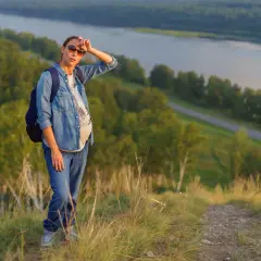 Donna in gravidanza, con zaino, su un sentiero di montagna a 1500 metri, con vista sul fiume.
