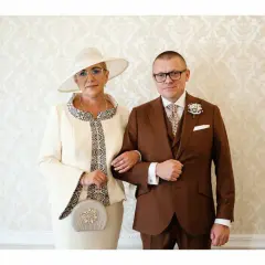 Elegancka mama pana młodego w kremowym kostiumie i kapeluszu, obok syna w brązowym garniturze.
