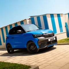 Voiturette bleue Ligier garée devant des cabines de plage rayées. Idéale pour la nouvelle loi voiture sans permis.
