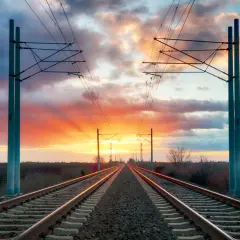 Torowisko kolejowe w zachodzącym słońcu. W oddali widać słupy trakcyjne, jeden z nich ma wskaźnik w3.