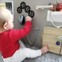Dziecko bawi się przy tablicy manipulacyjnej diy: zębatki, myszka, zamek, kłódka i pluszaki.