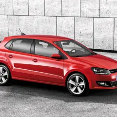 Czerwony Volkswagen Polo 6R z felgami aluminiowymi stoi na tle nowoczesnej, betonowej ściany.