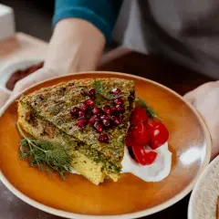 Une part de kuku sabzi, une tarte aux herbes persane, garnie de grenades et de tomates cerises, servie avec une touche de yaourt.