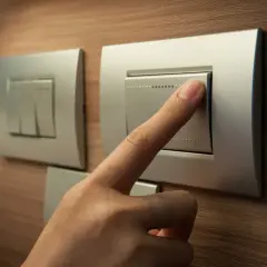 Dłoń naciska nowoczesne włączniki światła na drewnianej ścianie.