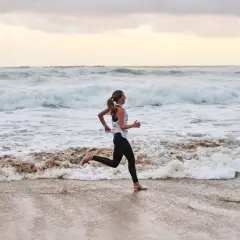 Frau joggt barfuß am Strand entlang, während die Wellen des Meeres an den Sand spülen. Sie genießt ihr tägliches Joggen.