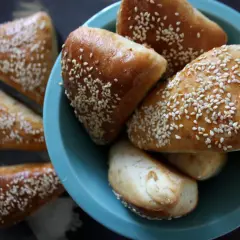 Gyllene trekanter i långpanna, toppade med sesamfrön, ligger i en turkos skål.