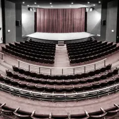 Pusta sala widowni w teatrze im. Aleksandra Sewruka w Elblągu, z rzędami czerwonych foteli i sceną w tle.