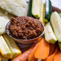 A bowl of savory miso dip is surrounded by fresh, colorful crudités: sliced zucchini, yellow squash, carrots, and cabbage wedges, ready for dipping.