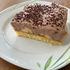 Ein Stück Bananen Torte mit Schokoladencreme und Schokostreuseln auf einem Teller mit Blattmuster.