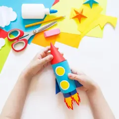 Dziecko tworzy rakietę z kartonu, używając kolorowego papieru, nożyczek i kleju. To świetny sposób, jak zrobić rakietę z kartonu!