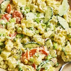 A creamy Japanese potato salad with chunks of potato, cucumber, peas, and carrots, garnished with green onions and black pepper.
