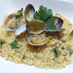 Piatto di fregola con vongole, profumata al prezzemolo e condita con un filo d'olio. Un classico della cucina sarda.