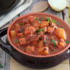 Un saporito polpo alla pignata, con patate e prezzemolo, servito in una ciotola di terracotta.