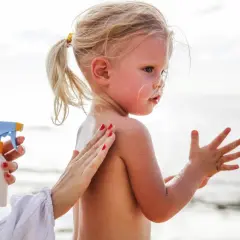 Ochrona przed słońcem jest kluczowa, by uniknąć oparzeń słonecznych u dzieci. Mama smaruje córkę kremem na plaży.