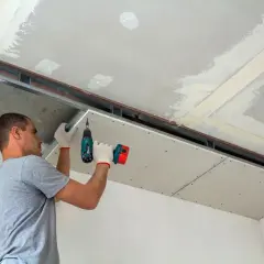 Mężczyzna montuje płyty gipsowo-kartonowe na suficie, przygotowując go do nałożenia gładzi.
