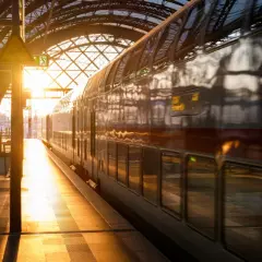 Złote światło wschodu słońca oświetla peron i pociąg PKP. Widok na dworzec kolejowy z pociągiem dwupoziomowym.
