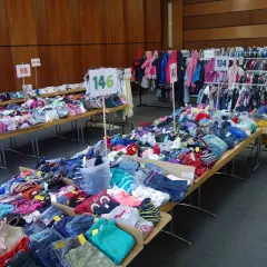 Großer kinderflohmarkt in Bergisch Gladbach mit Kleidung auf Tischen und Kleiderstangen.