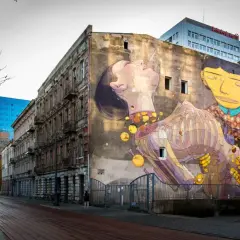 Imponujące street art na ścianie kamienicy, przedstawiające surrealistyczną scenę z postaciami i elementami anatomicznymi.