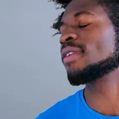 Un homme avec une barbe collier épaisse, les yeux fermés, porte un t-shirt bleu vif.