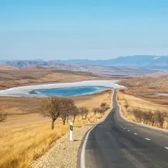 Droga przez gruzińskie krajobrazy, z zamarzniętym jeziorem i górami w tle. Idealne miejsce na podróż z gruzińskim prawem jazdy.