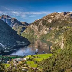 Majestätische fjorde norwegen, mit einem Kreuzfahrtschiff auf dem ruhigen Wasser, umgeben von steilen, grünen Bergen und einem kleinen Dorf.