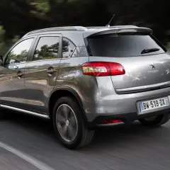 Srebrny Peugeot 4008 jedzie po drodze wśród drzew.