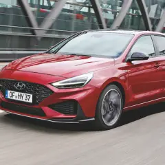 Czerwony Hyundai i30 2024 w wersji N Line pędzi po drodze, z nowoczesną atrapą chłodnicy i ostrymi światłami LED.