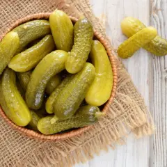 Koszyk pełen kiszonych ogórków na jutowym płótnie. Zastanawiasz się, ile kcal ma ogórek kiszony? To zdrowa przekąska!