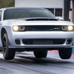 Srebrny Dodge Challenger SRT na torze wyścigowym, z przednimi kołami lekko uniesionymi nad asfaltem.