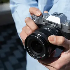 Dłonie trzymające srebrny aparat Fujifilm X-T50 z obiektywem Fujinon.