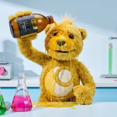 Ein Teddybär kippt eine Flasche Vitamin C über sich. Sieht aus, als hätte er zu viel Vitamin C genommen und nun klebt alles.