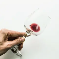 Mano che tiene un bicchiere di vino rosso, con un residuo che ricorda l'acido tartarico, essenziale per la sua conservazione.
