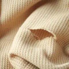 Uszkodzony beżowy sweter z dziurą. Dowiedz się, jak zacerować dziurę w swetrze, by znów był jak nowy.