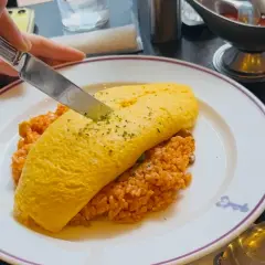 A knife cuts into a fluffy omelet atop rice, a delicious example of Japanese dishes with cheese.