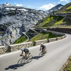 Dwóch kolarzy pokonuje serpentyny na przełęczy Stelvio, otoczeni surowym, górskim krajobrazem.