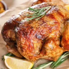 Un poulet rôti doré, garni de romarin et de quartiers de citron, prêt à être dégusté après une cuisson parfaite à 150 degrés.