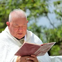 Kapłan w białej albie zamyślony nad księgą, w której widnieje napis "Modlitwa żal za grzechy".