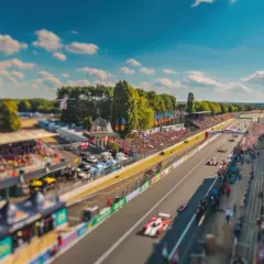 Wyścig na torze Le Mans. Tłumy kibiców na trybunach, bolidy pędzące po asfalcie pod błękitnym niebem.