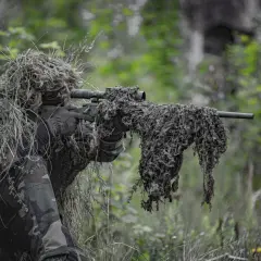 Un francotirador camuflado en un bosque, listo para la acción. El airsoft, un deporte que simula combates, requiere sigilo y estrategia.