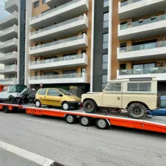 Laweta z autami: żółty Twingo, biały terenowy i beżowy Land Rover. B+E DMC.